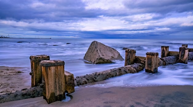 Dramatic view of a weathered breakwater and ocean waves under cloudy skies.