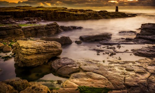 A rocky shore with a lighthouse in the distance