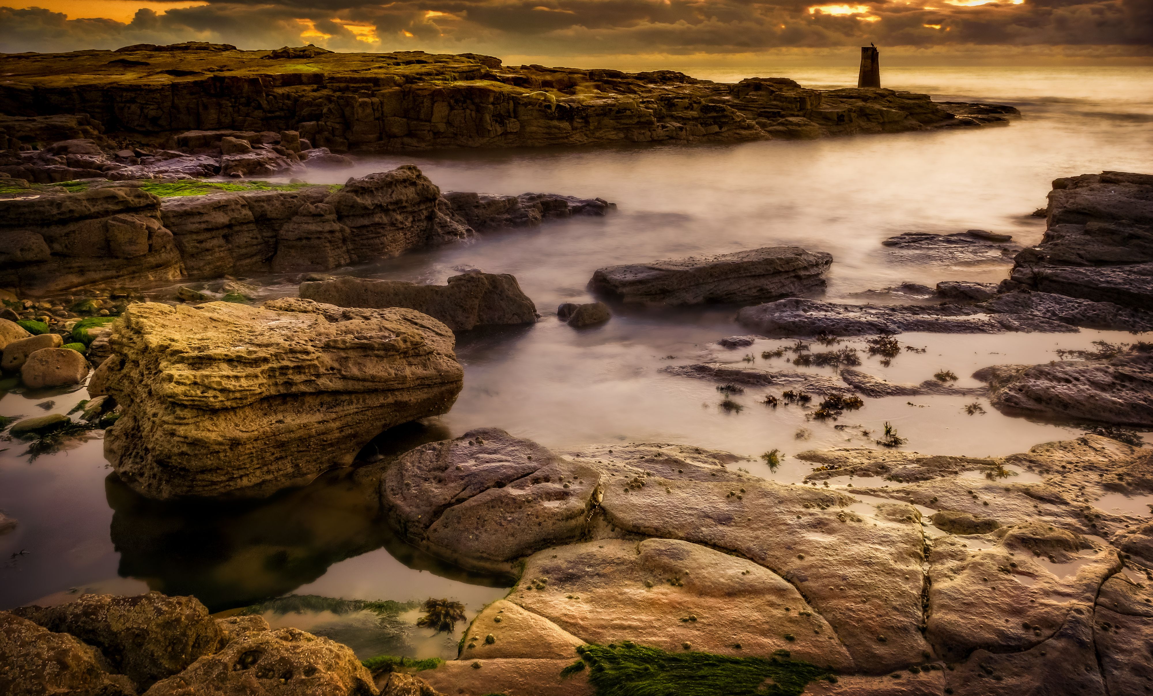 A rocky shore with a lighthouse in the distance · Free Stock Photo