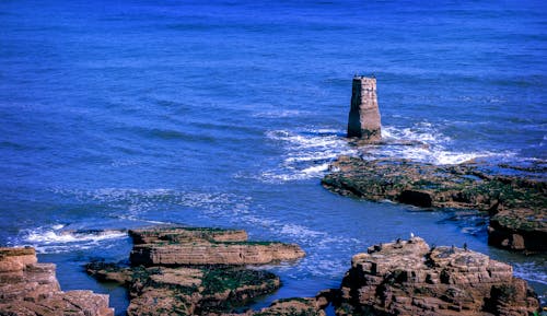 A lighthouse is on the rocks in the ocean