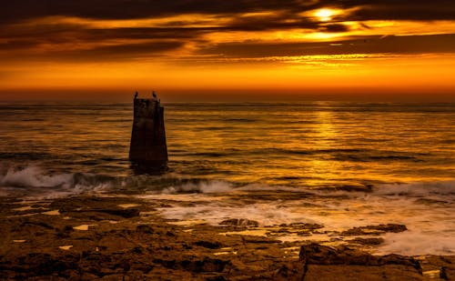 A lighthouse is silhouetted against the sunset