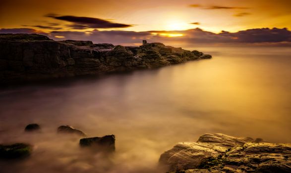 A tranquil seaside landscape captures the golden sunset lighting up the coast.