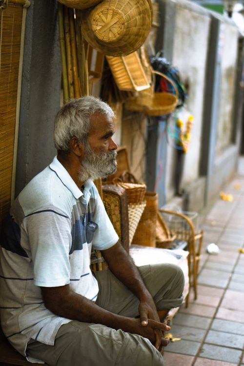 Free An elderly Indian man with a beard sitting by baskets in a city street market. Stock Photo