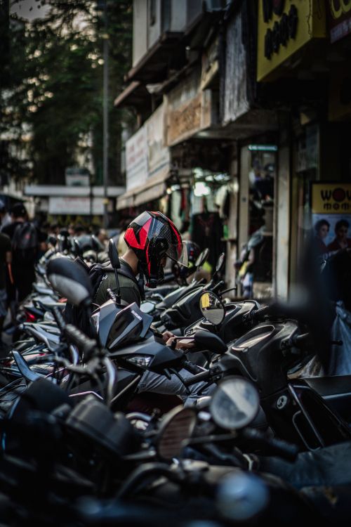 Free A row of parked motorcycles lined up on a busy urban street with a rider wearing a helmet. Stock Photo