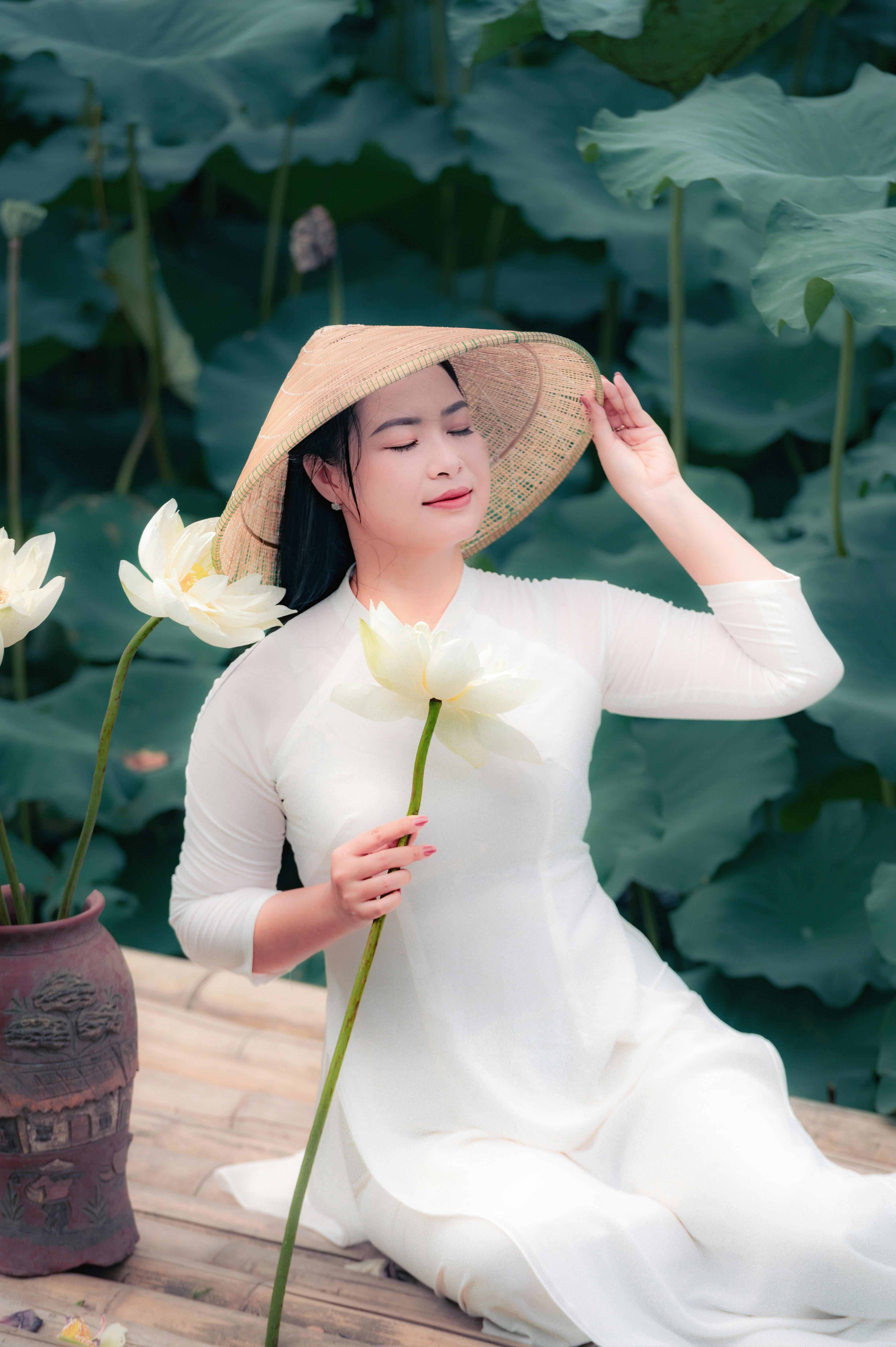 Asian woman in traditional dress with hat, sitting serenely among lotus flowers. Perfect for peaceful and cultural theme
