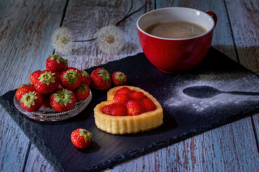 A heart-shaped strawberry tart with coffee on a rustic wooden table, perfect for indulgence.