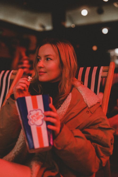 Free A woman sitting in a chair with a popcorn and a drink Stock Photo