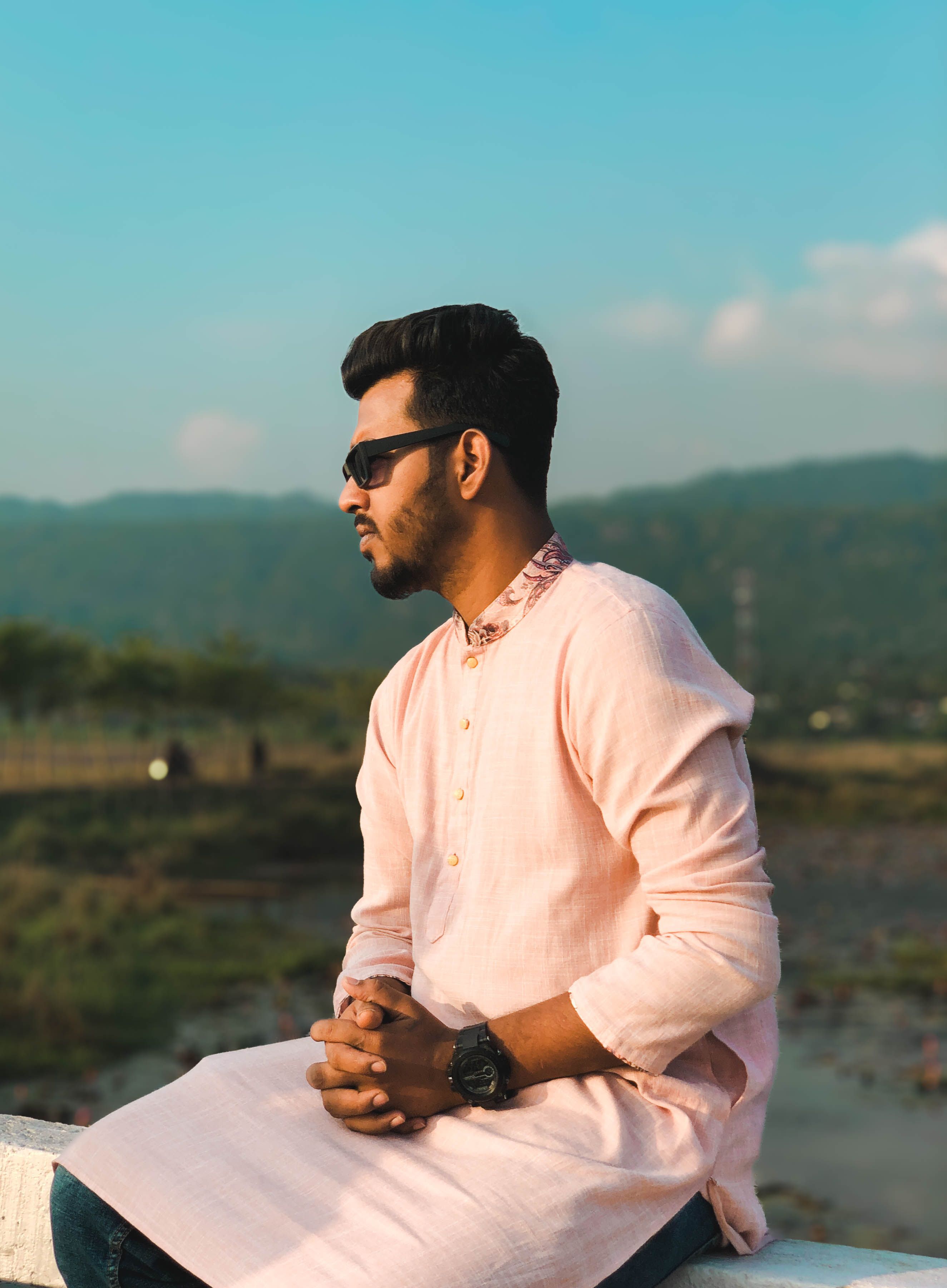 Portrait of a man in sunglasses wearing a kurta, sitting peacefully outdoors.