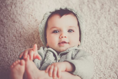 婴儿躺在地毯上的灰色针织连帽的衣服
