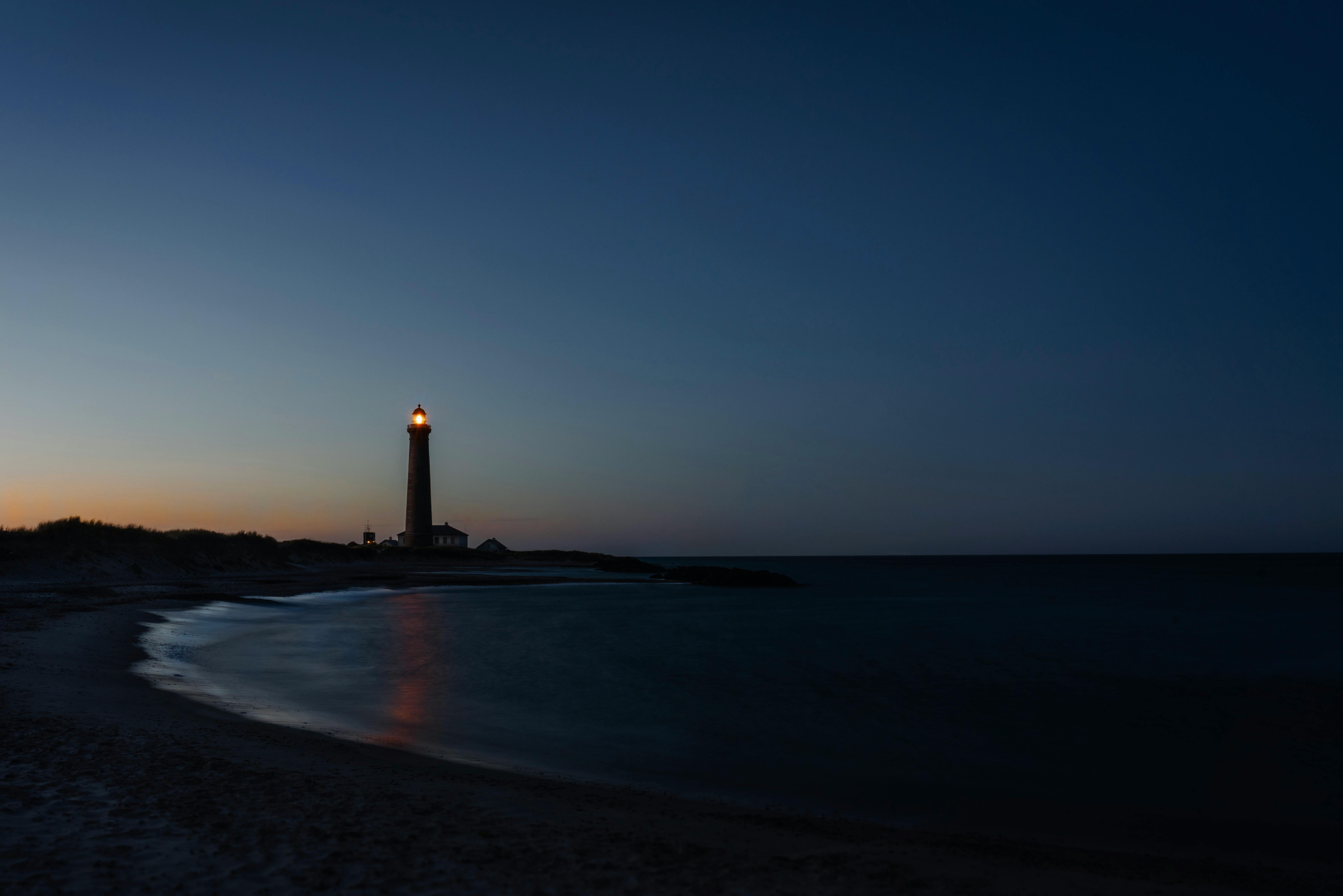 Peaceful view of Skagen Lighthouse at sunset with calm ocean waves and dusky sky.