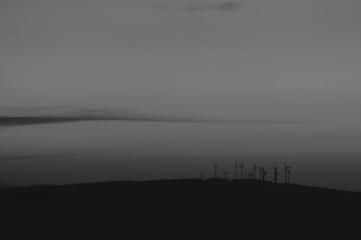 Monochrome image of wind turbines on a hill silhouetted against a twilight sky.