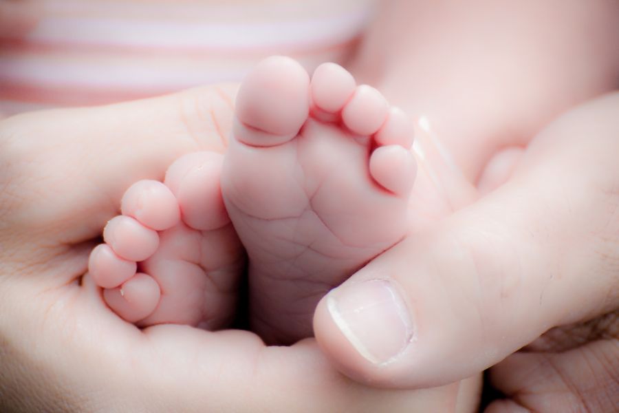 A newborn baby's feet gently cradled in an adult's hands.