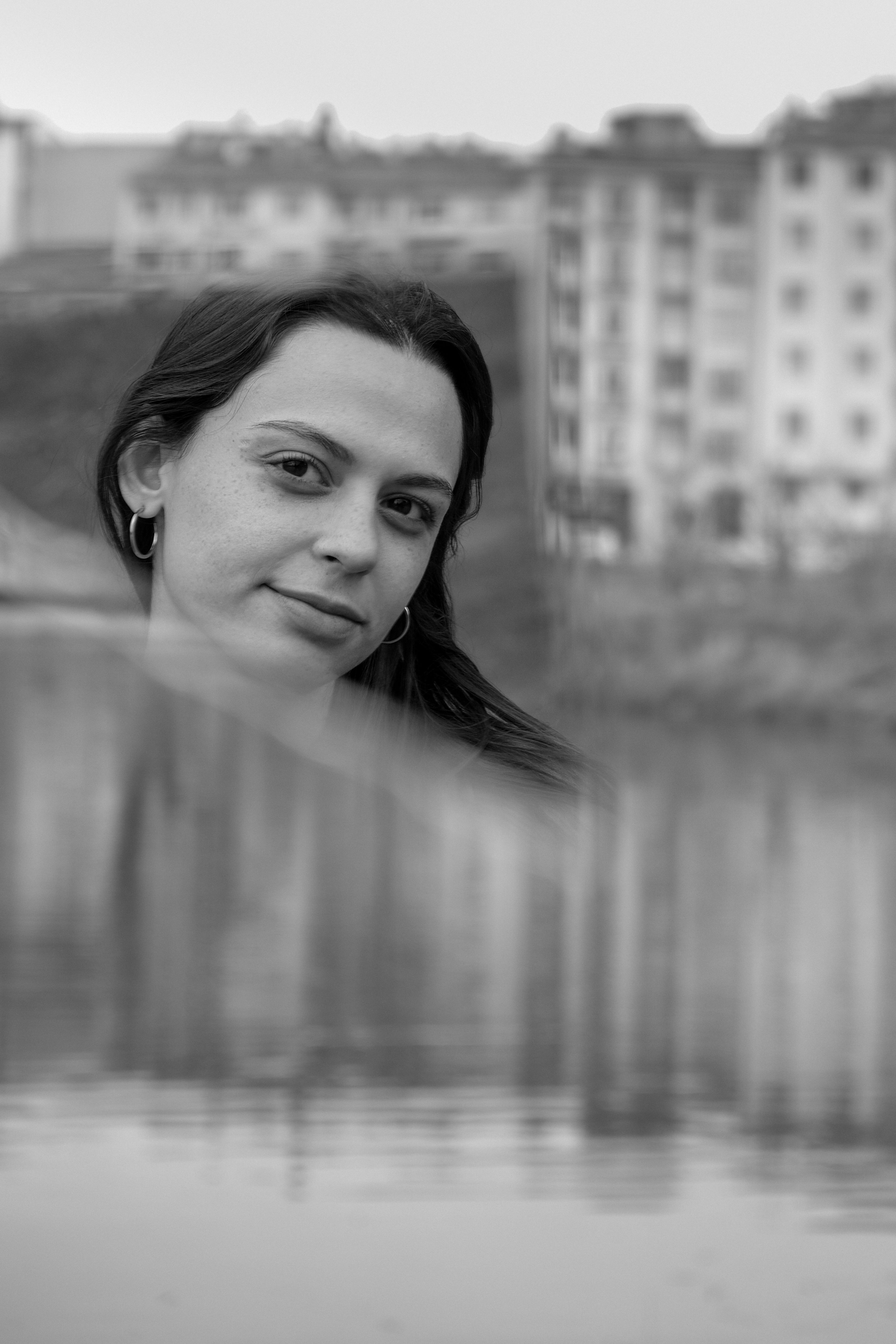 Black and white portrait of a woman with urban buildings in background reflection.