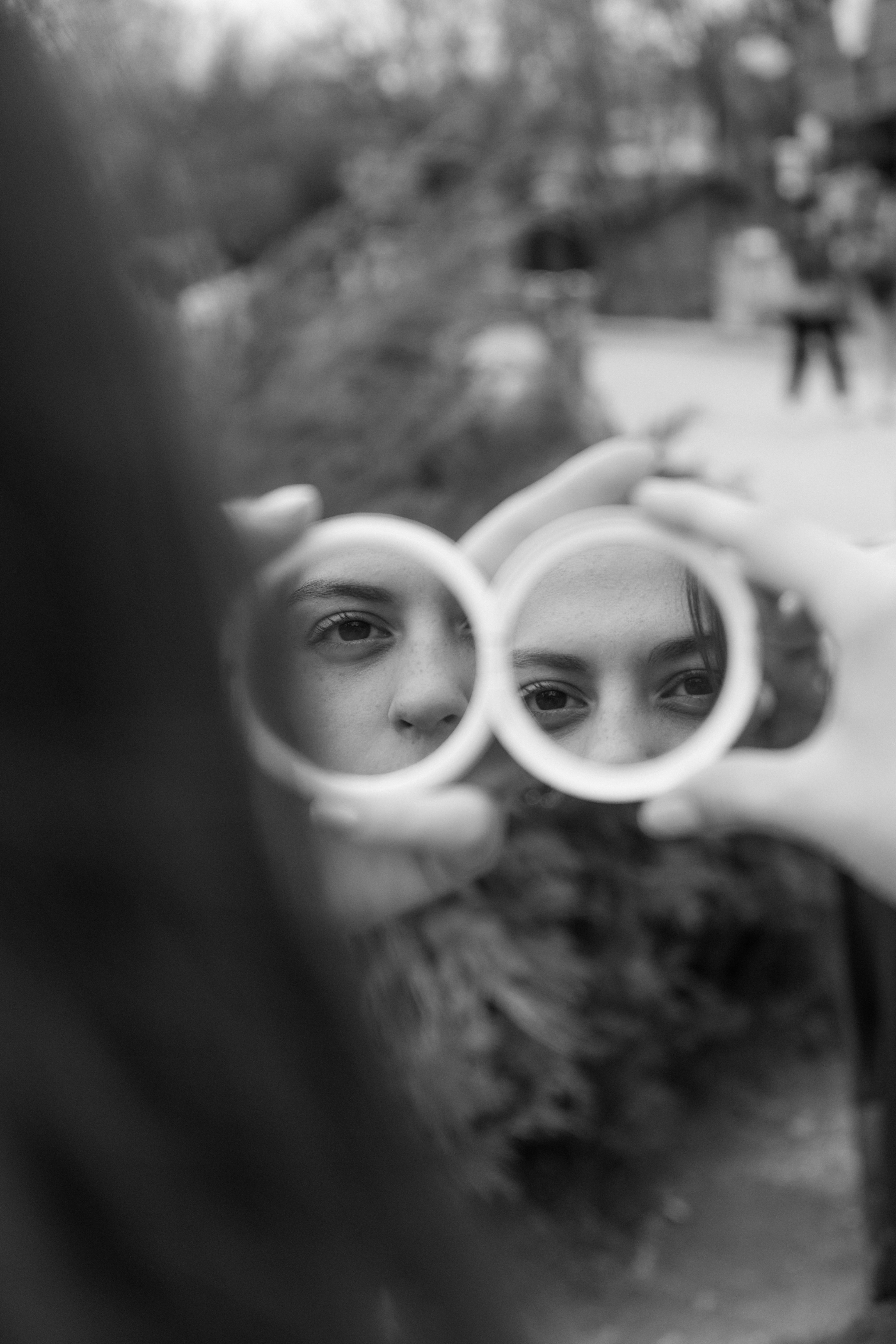 Black and white photo capturing a woman's reflection in mirrors outdoors.
