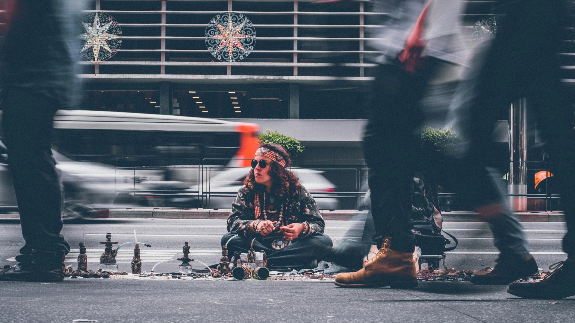 A street vendor sits with handmade crafts amidst bustling city traffic, capturing urban life.