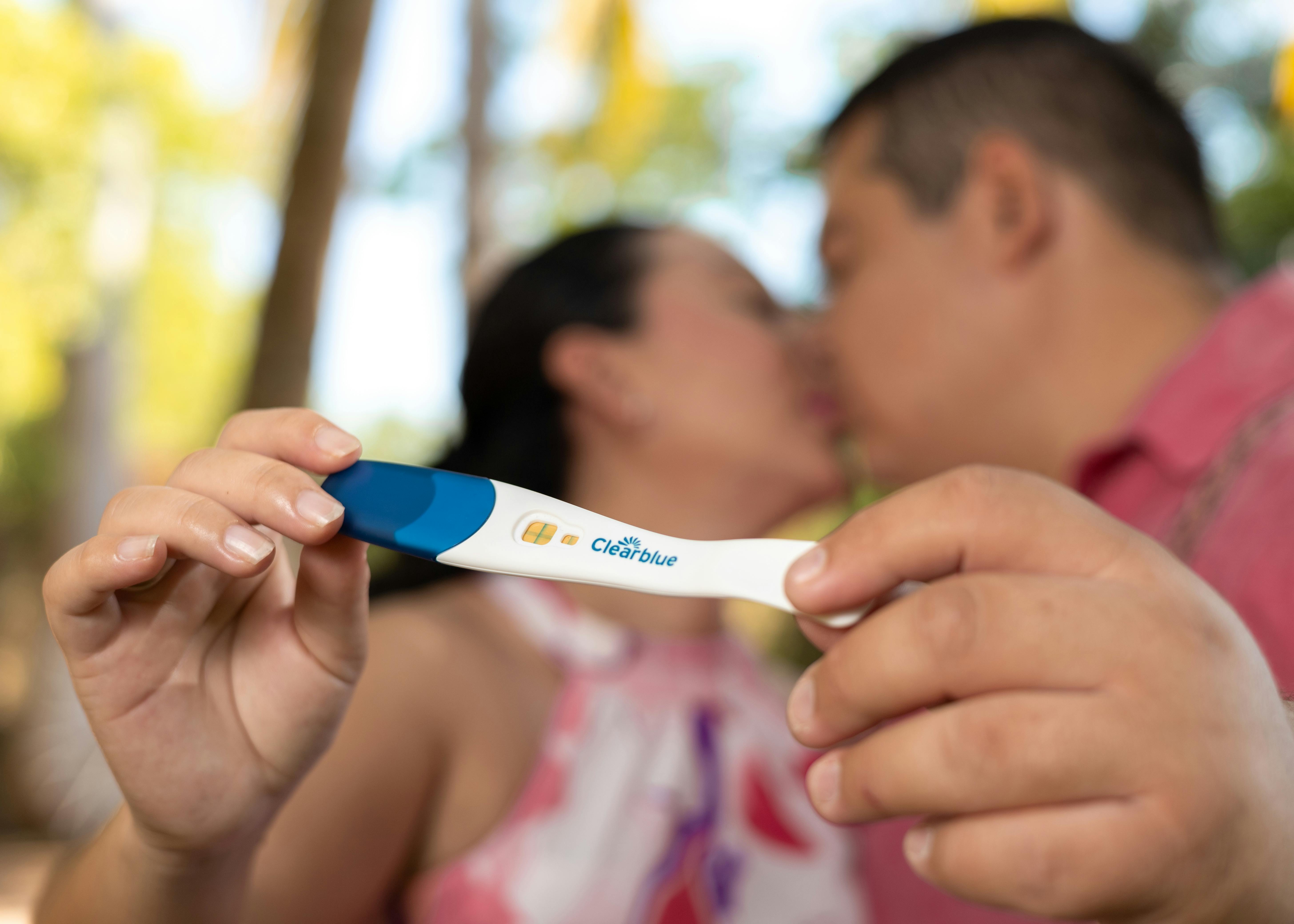 kissing couple holding positive pregnancy test