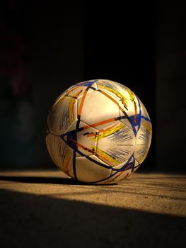 Colorful soccer ball resting in dramatic sunlight, highlighting its vibrant patterns.