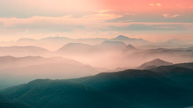 Serene view of misty mountains at dawn with warm colors and a tranquil atmosphere.