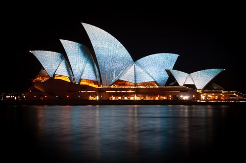 Free Stunning night view of the Sydney Opera House with illuminated sails, reflecting in the harbor. Stock Photo