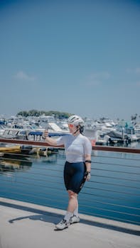 A woman cyclist in sportswear taking a selfie at a marina with boats on a sunny day.