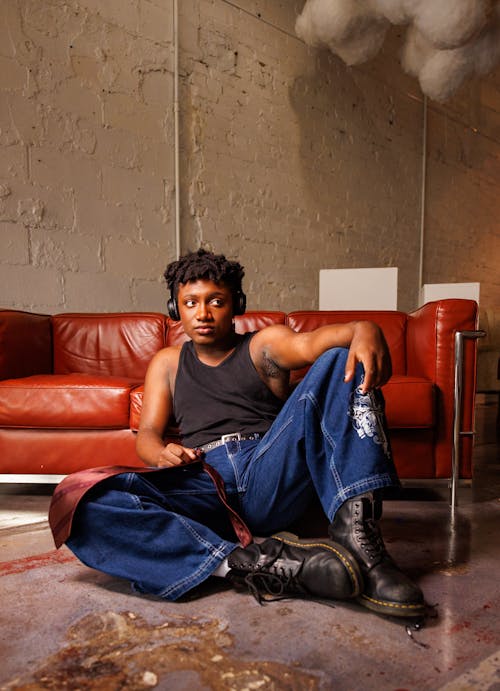 Free A Young Man in Jeans and a Tank Top Sitting by the Sofa Stock Photo