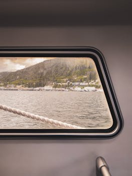 Capture of a coastal town landscape seen through a ship's window, highlighting serene waters.