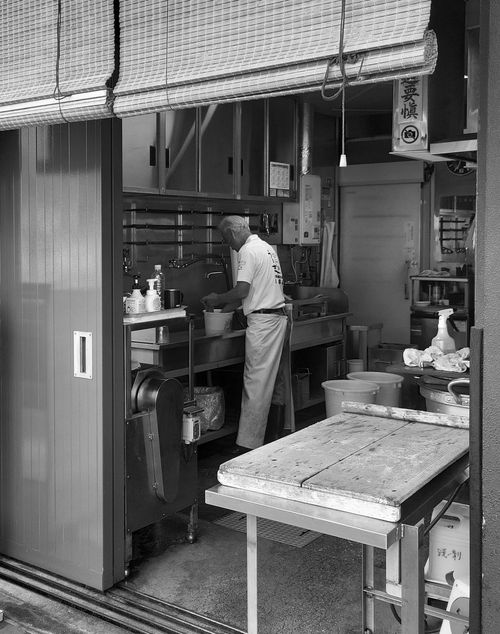 Free An elderly man cooking in a small street booth's kitchen, captured in black and white. Stock Photo
