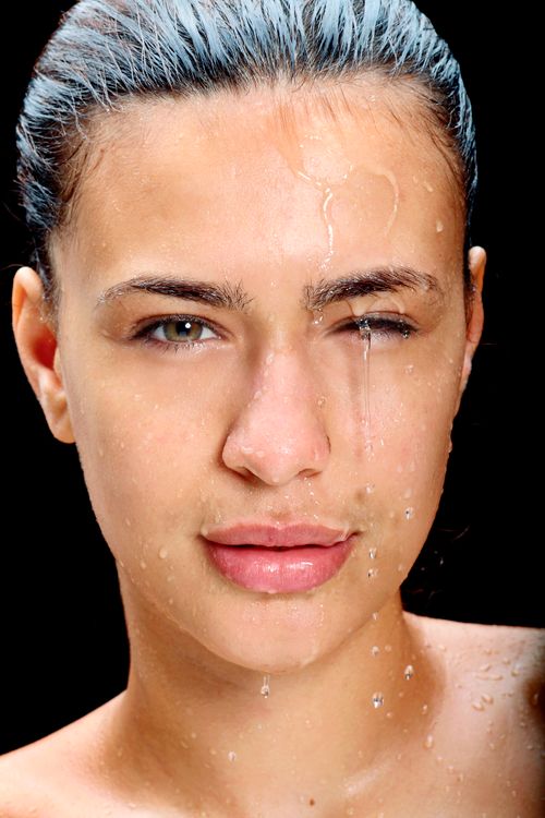 Free Close-up portrait of a wet woman with water droplets on her face, set against a dark background. Stock Photo