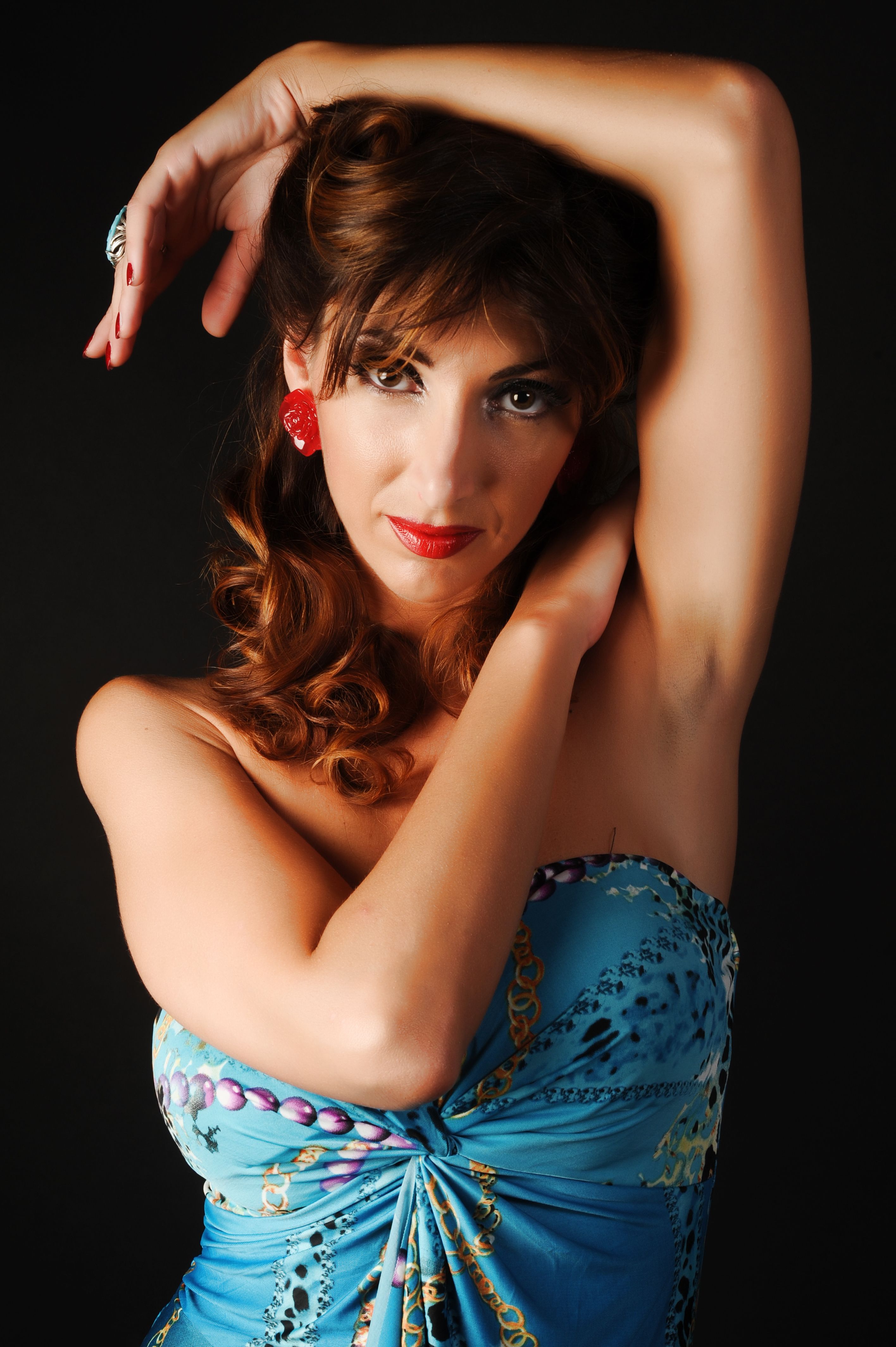A fashion studio portrait of an elegant woman in a blue dress with arms raised.