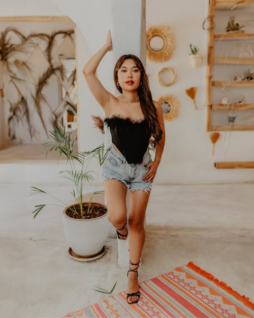 A woman in a black top and shorts posing in front of a plant