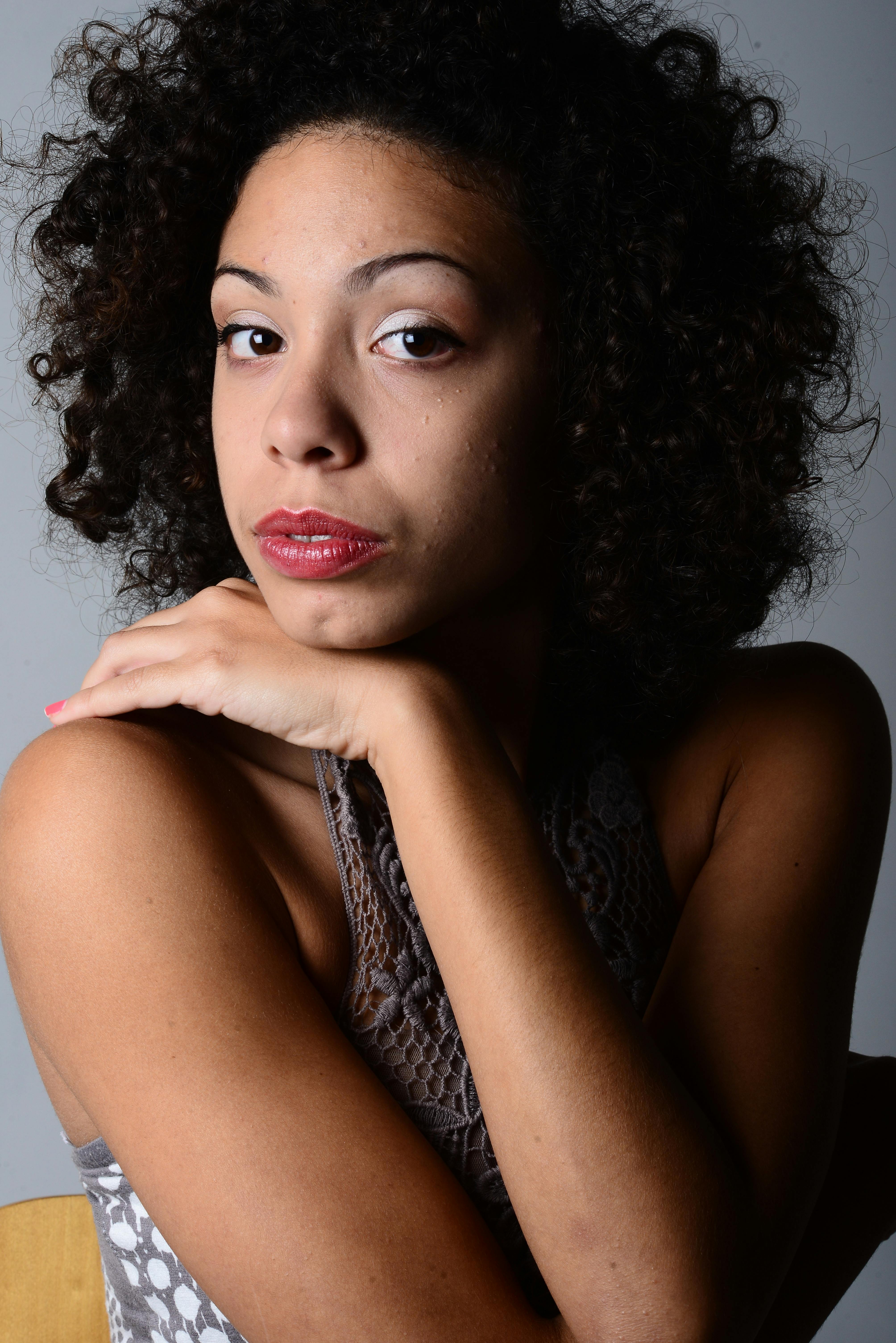 Striking studio portrait of a woman with curly hair and a contemplative pose.