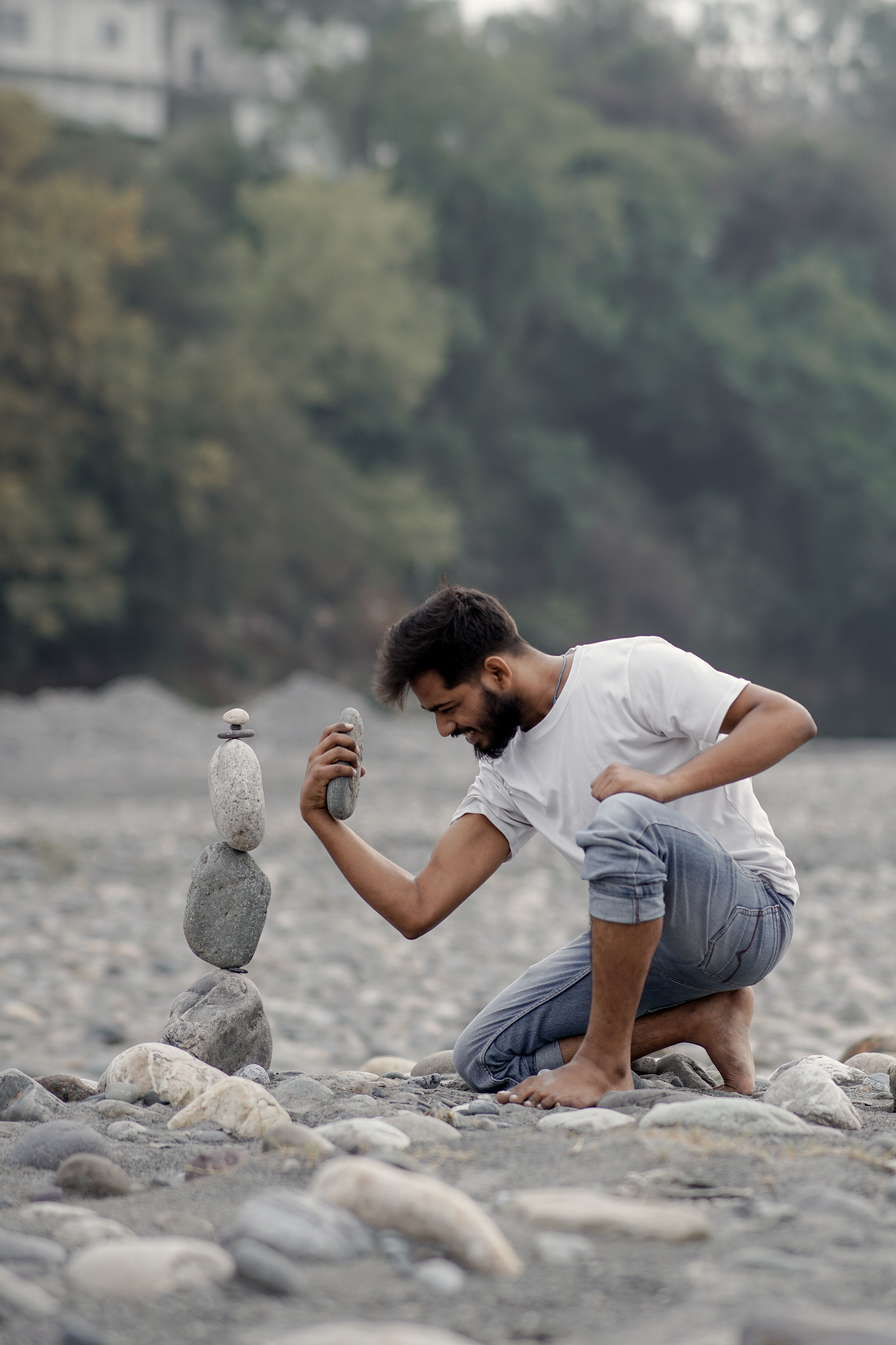 A man carefully balances stones outdoors, creating a zen-like structure in nature.