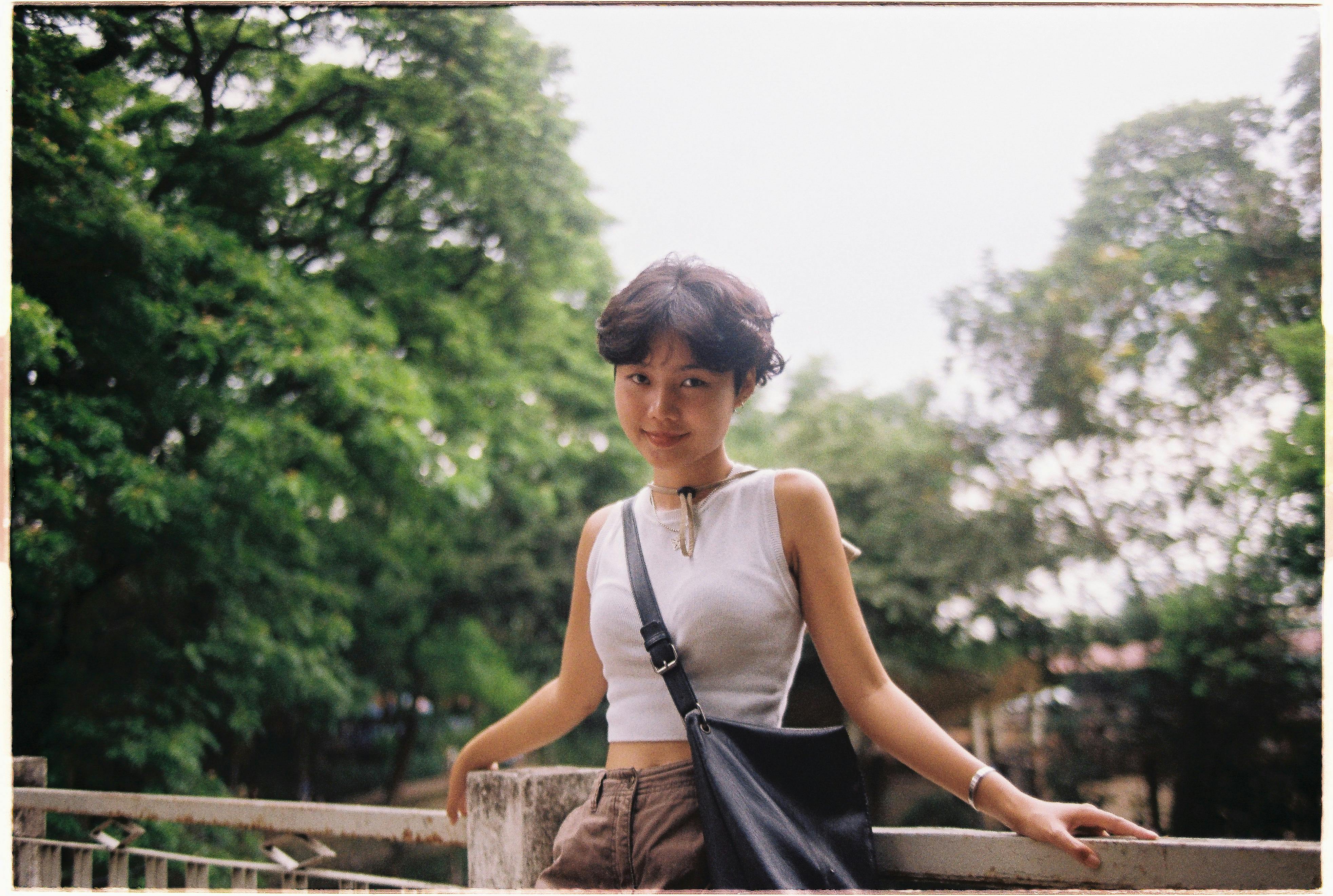 A young woman stands on a bridge in Ho Chi Minh City, enjoying a summer day.