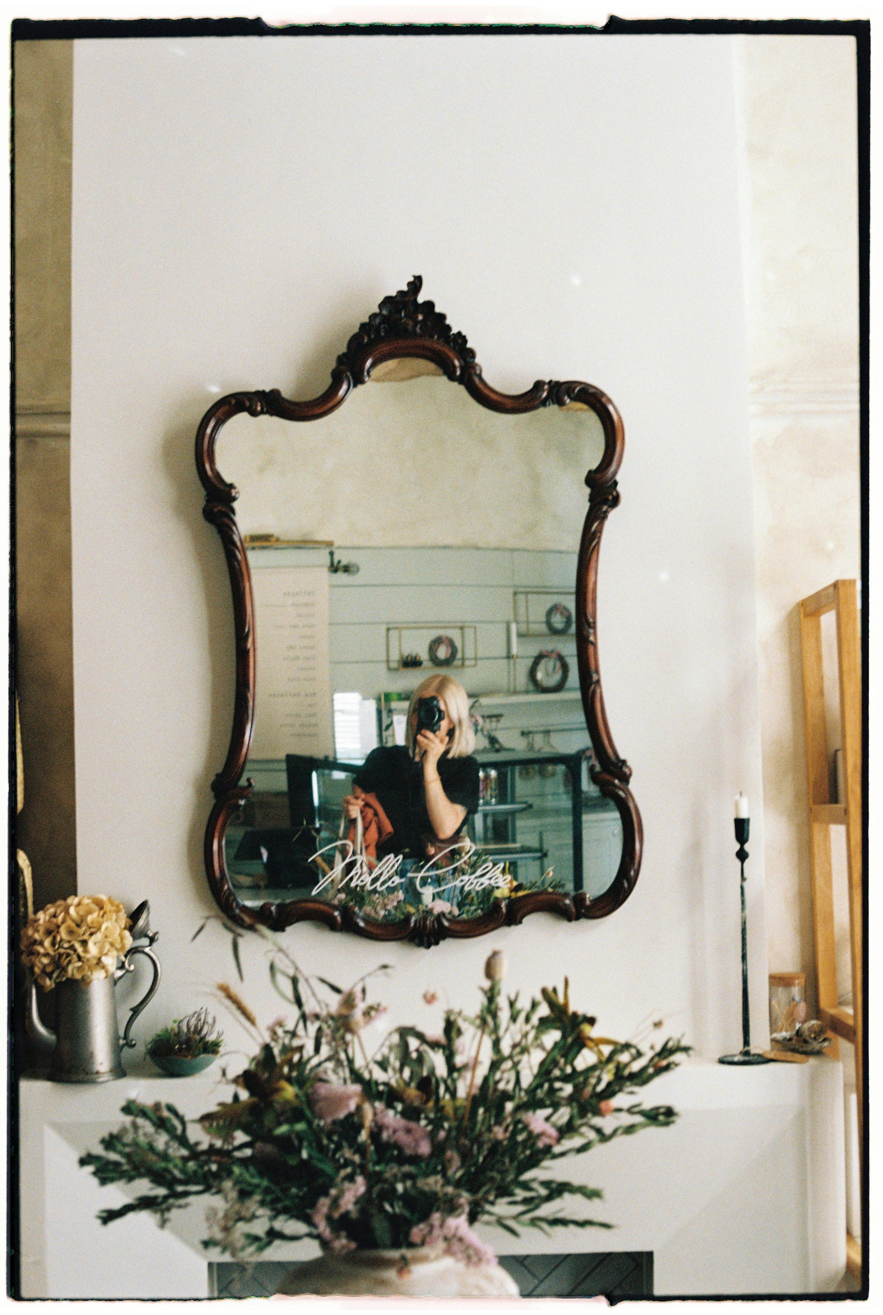 Artistic reflection of a woman in a vintage mirror with flowers and decor.