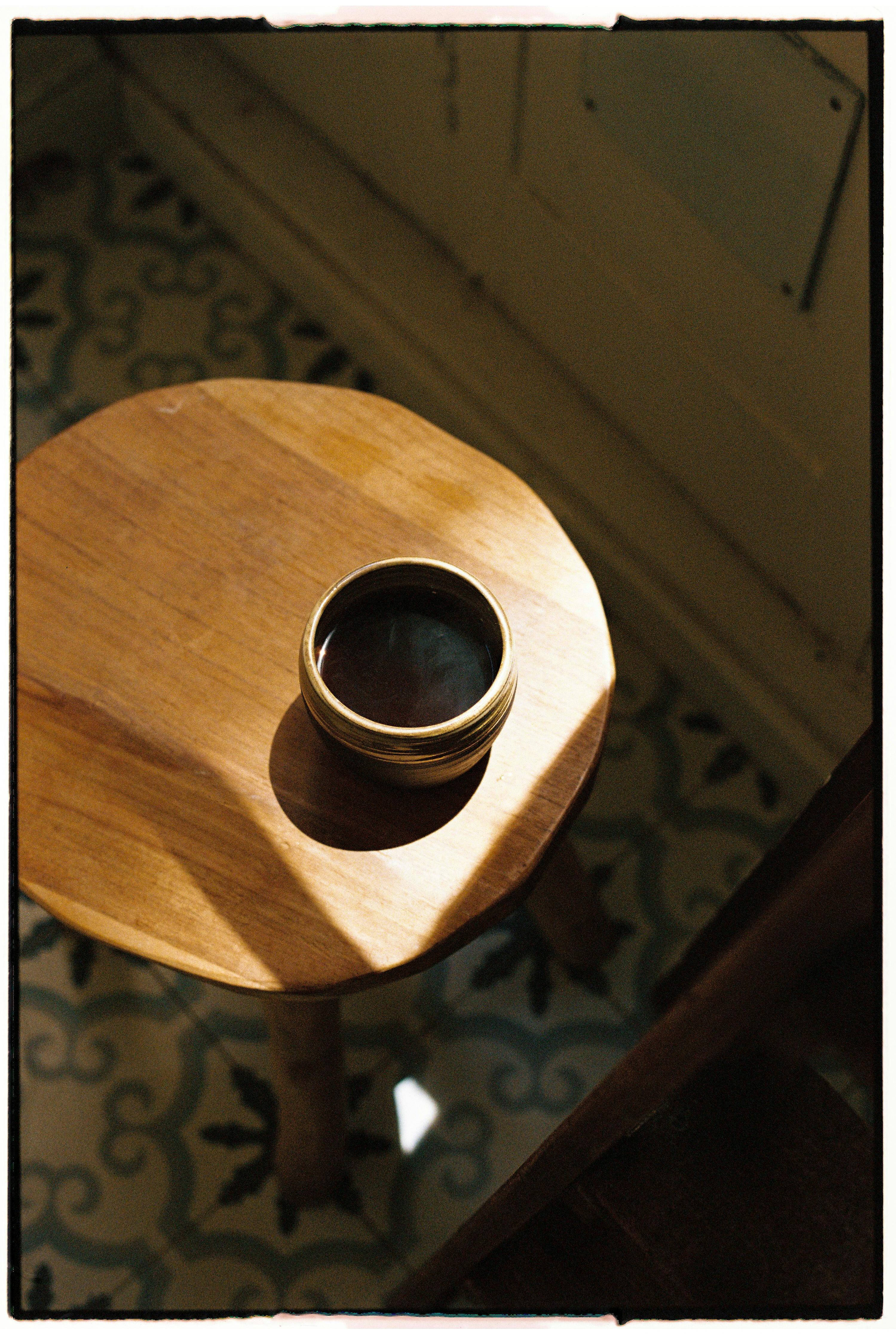 Cup of coffee casting shadow on wooden stool, highlighting cozy ambiance.