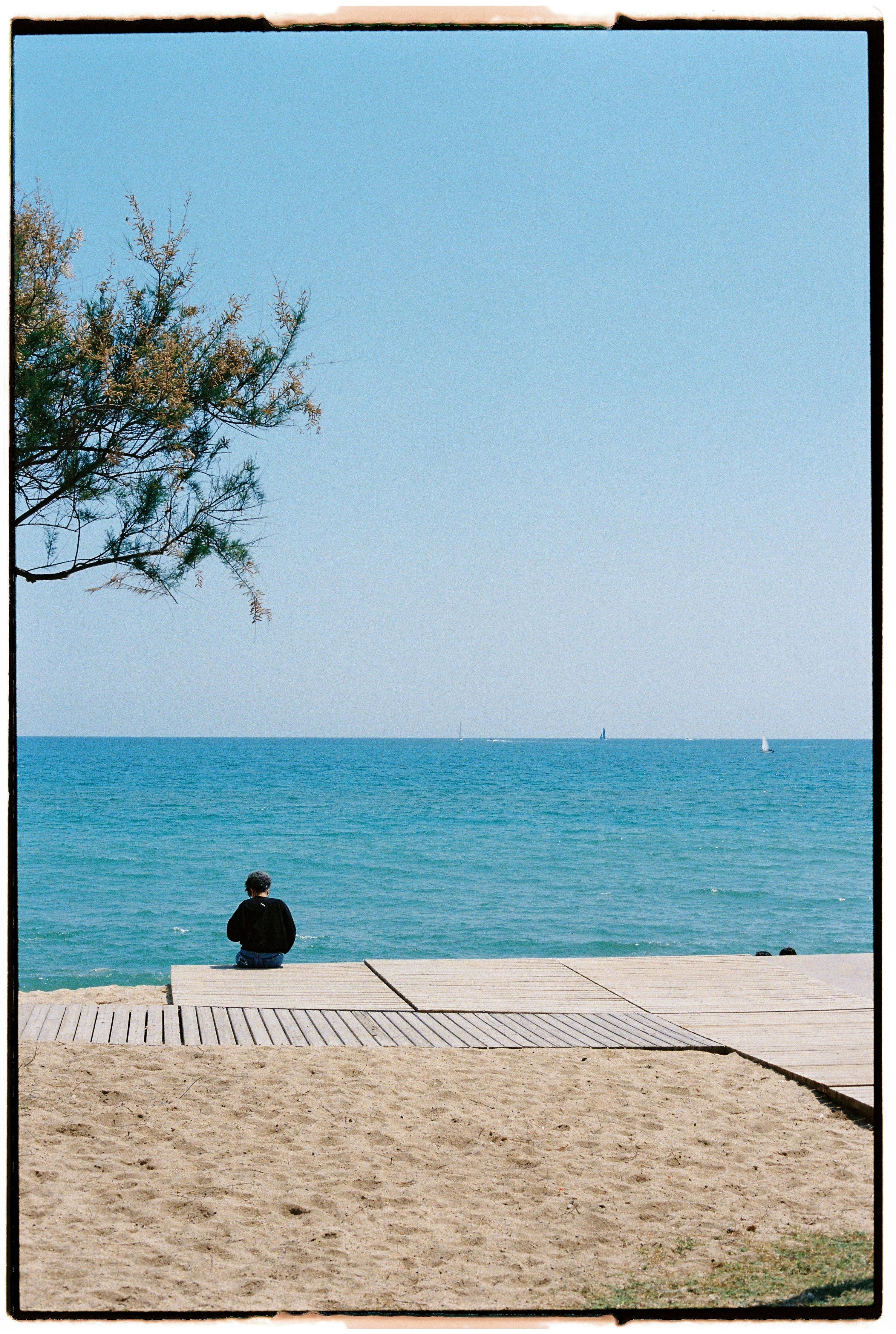 Person relaxing by the sea on a sunny day, enjoying clear skies and ocean views.