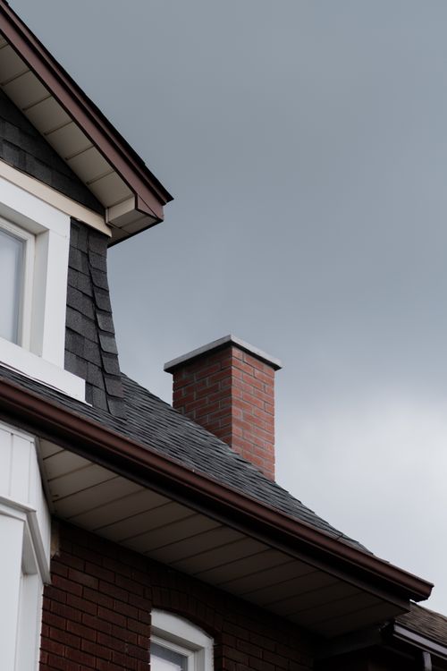 Free Close-up of a house roof with a brick chimney against a cloudy sky. Stock Photo
