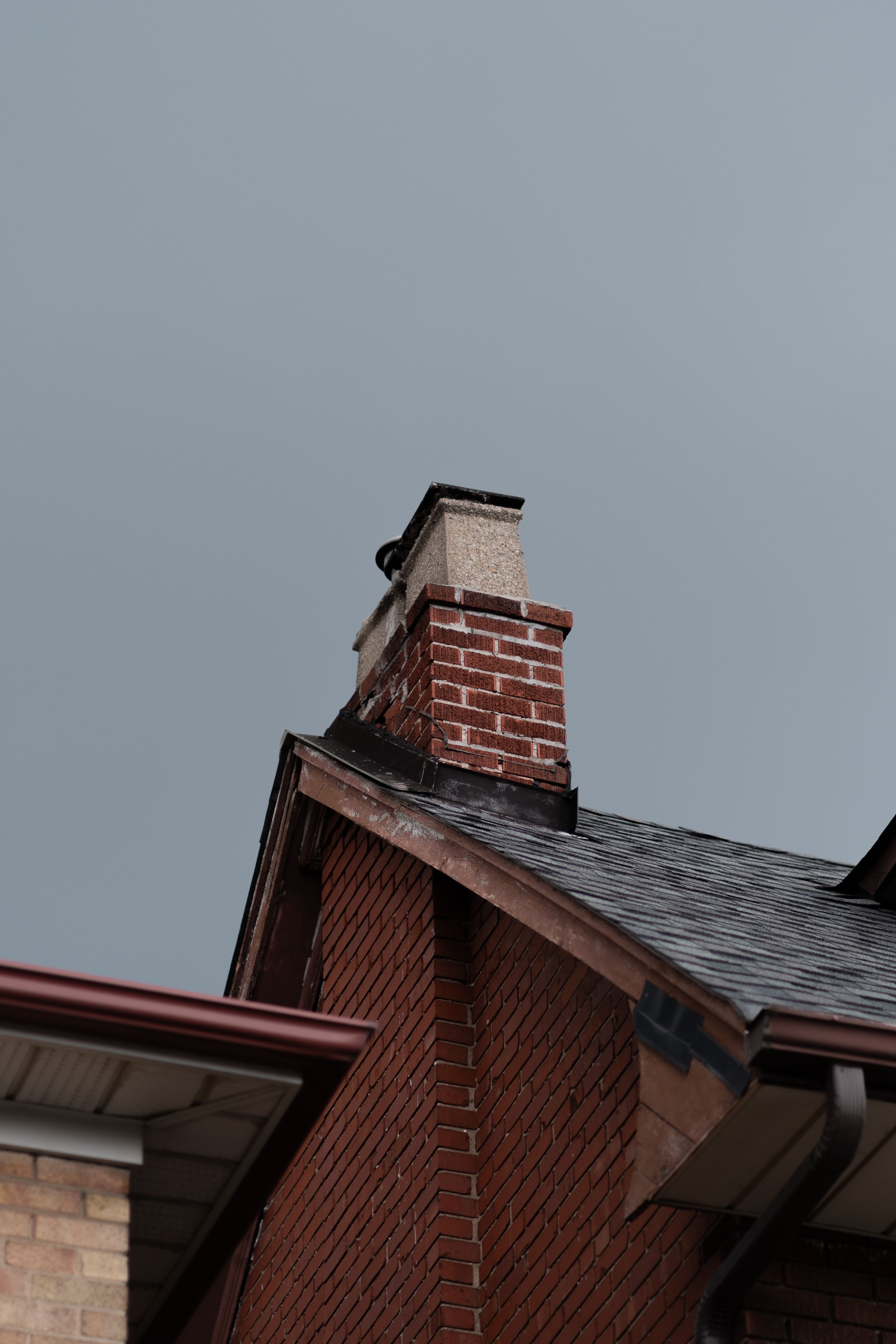 Brick chimney on a residential roof with visible metal flashing where it meets the shingles