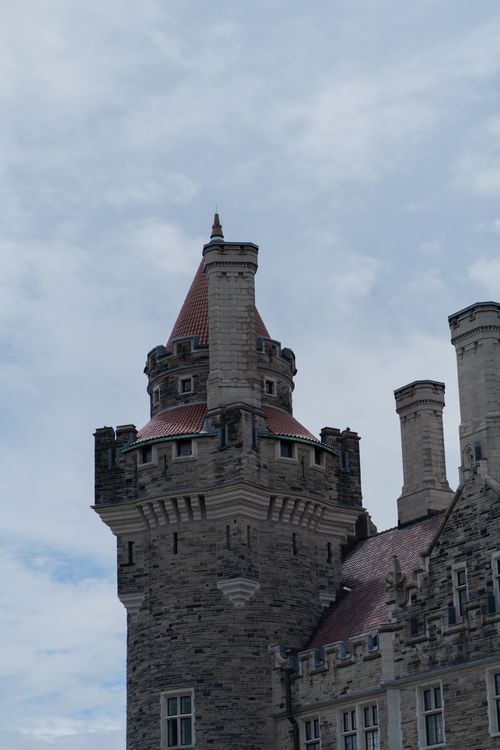 Free Close-up of a historic castle tower with brick turrets and chimneys under a cloudy sky. Stock Photo