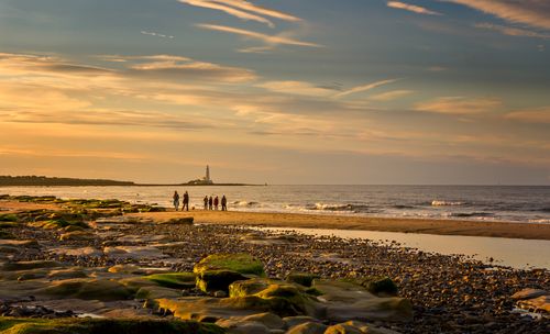 Free Peaceful sunset scene with people walking on the beach near a lighthouse. Stock Photo