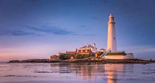Free Beautiful lighthouse on an island reflecting in the water during sunset. Stock Photo
