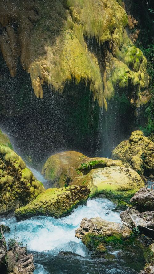 Free Enchanting waterfall with moss-covered rocks and splashing stream in natural setting. Stock Photo