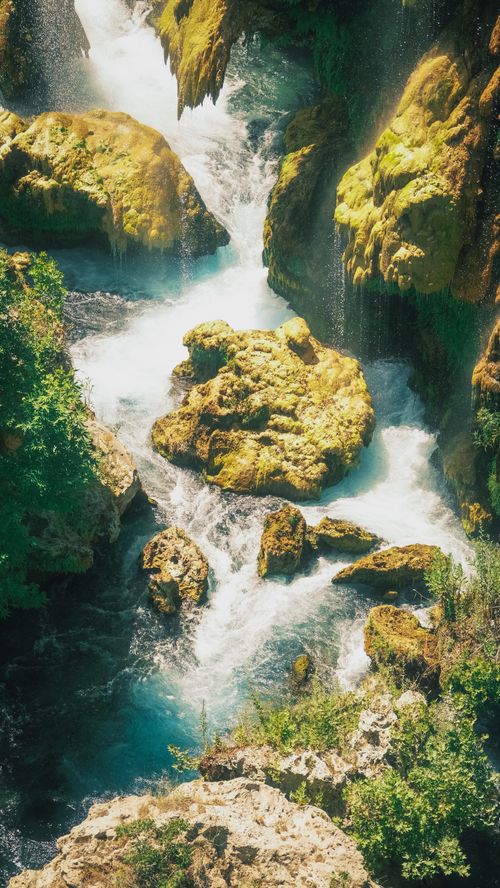 Free A picturesque view of a waterfall cascading over vibrant moss-covered rocks in a lush, natural setting. Stock Photo