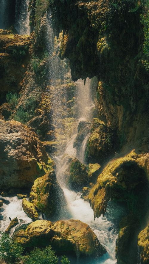 Free A breathtaking vertical shot of a waterfall cascading over moss-covered rocks in a natural setting. Stock Photo