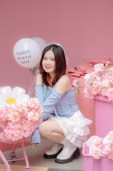 Smiling girl celebrating her birthday indoors with balloons and pink flowers.