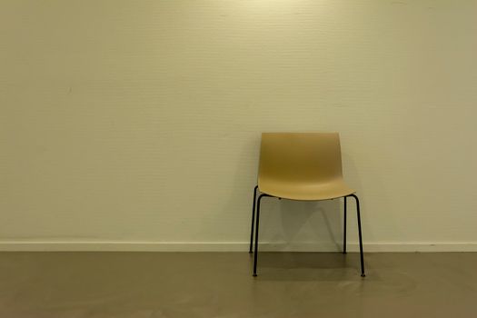 A solitary chair placed against a plain wall in a minimalistic setting, ideal for concepts of isolation and simplicity.