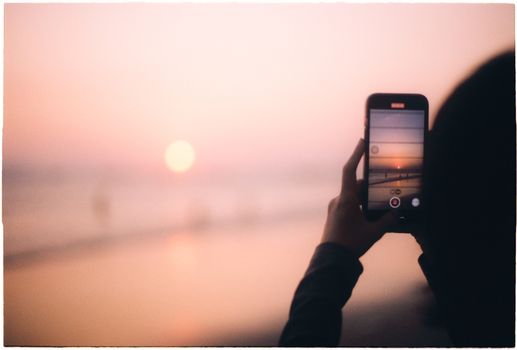 A silhouette captures the vibrant Vũng Tàu sunset on a beach via smartphone.
