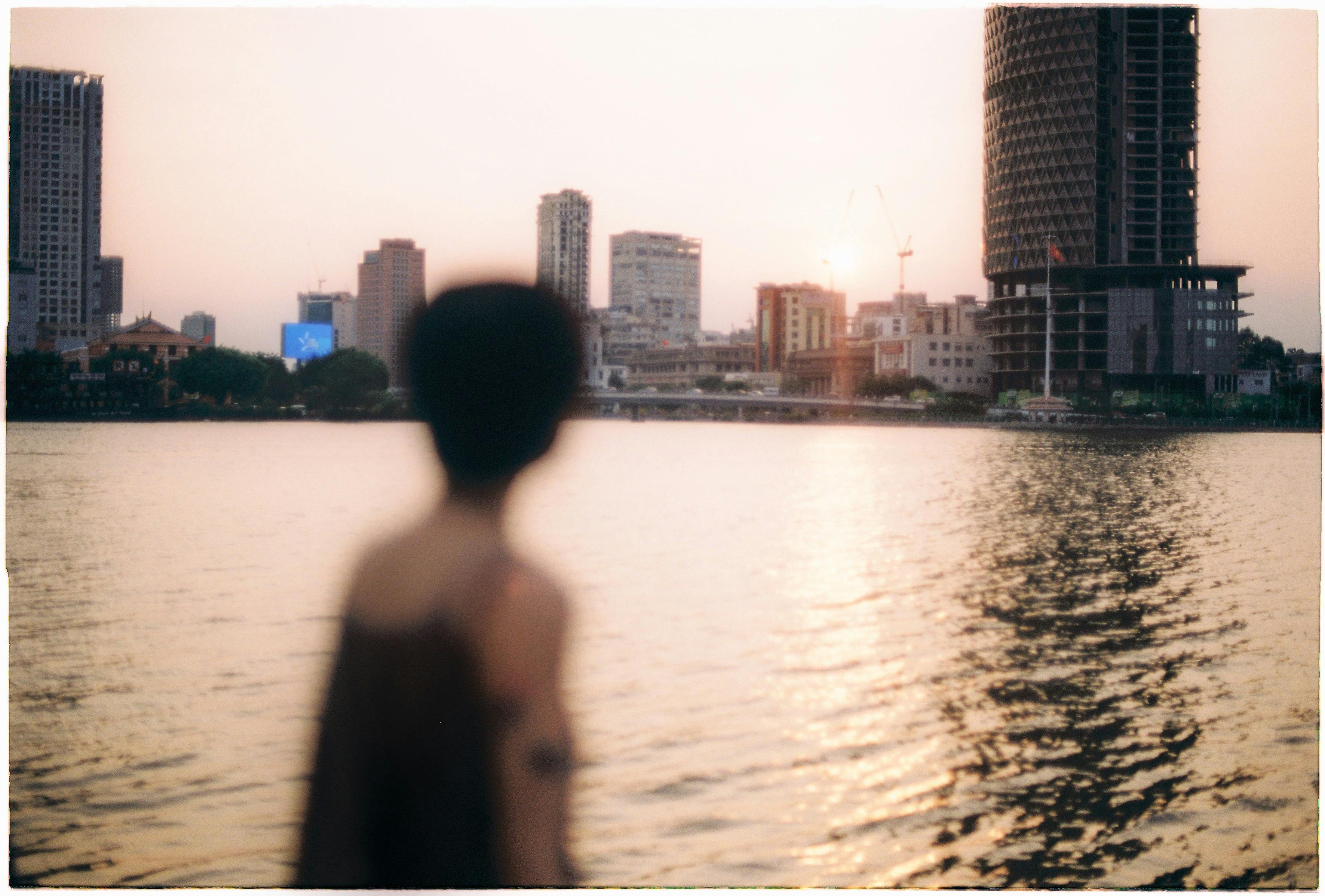 Silhouette of a person overlooking the waterfront with Ho Chi Minh City's skyline at sunset.