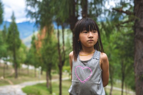 Free Portrait of a young girl in a gray tank, standing amidst lush trees in Bhutan. Stock Photo