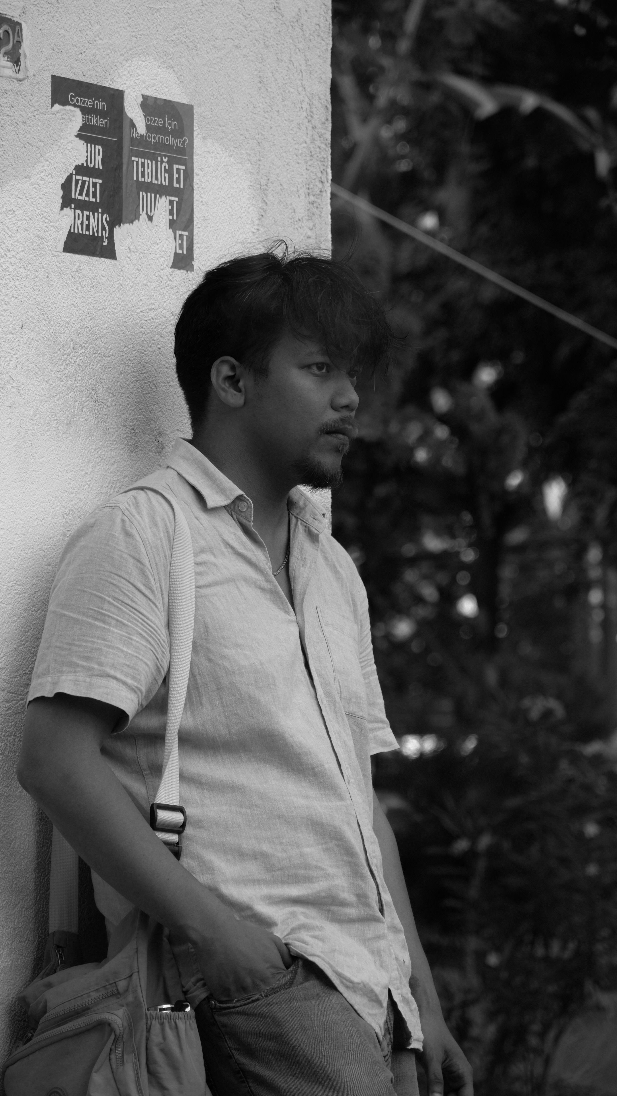 Black and white portrait of a contemplative man leaning against a wall outdoors.